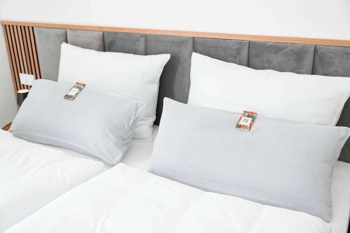 A neatly made bed with white linens and two pillows, a wooden headboard, and a bedside table with a lamp.