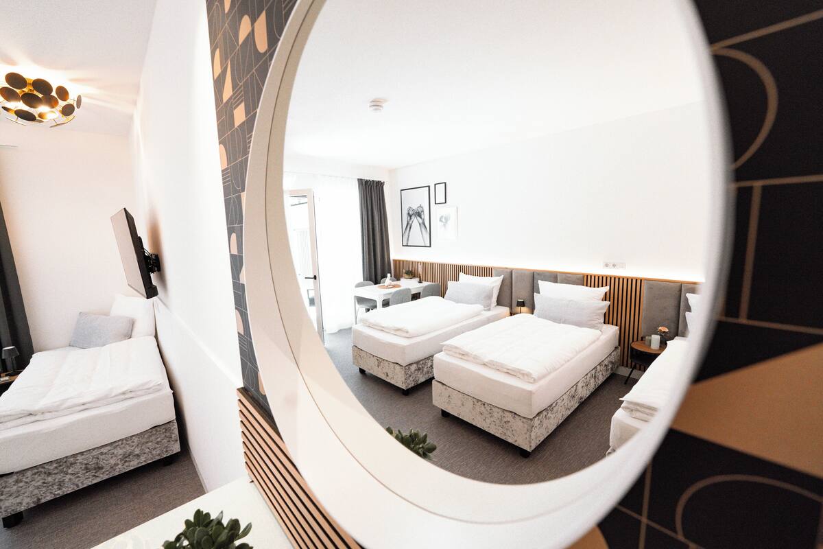 A hotel room with two beds, a desk, a chair, and a mirror reflecting the room.