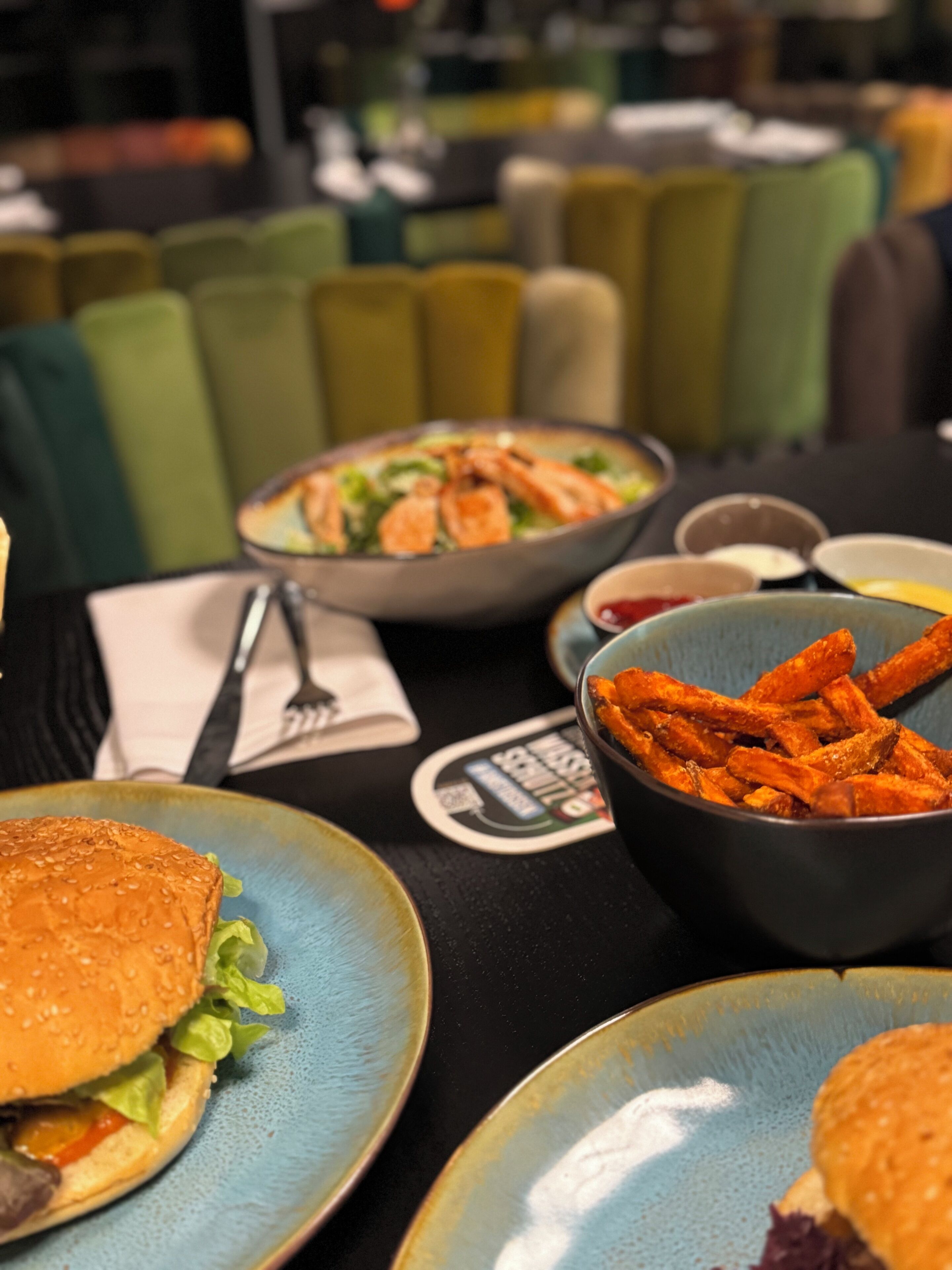 Un restaurante con una mesa dispuesta para una comida, que incluye una hamburguesa, un tazón de papas fritas y un tazón de ensalada.