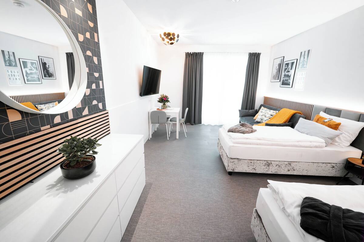 A modern hotel room with a large bed, a desk, a chair, a TV, and a potted plant.