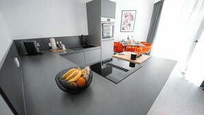Et moderne køkken med en central ø, indbygget ovn og spiseplads med orange stole.