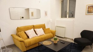 A living room with a mustard-colored sofa, a black armchair, a coffee table with a plant, a mirror, and a radiator. - Pez's newly renovated house! (Roma)