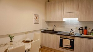A compact kitchen with light wood cabinets, a black countertop, a sink, and a stove. There is a small dining area with a white table and chairs. - Pez's newly renovated house! (Roma)
