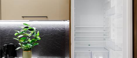 A kitchen with a marble countertop, a black coffee maker, a green plant, and a modern refrigerator.