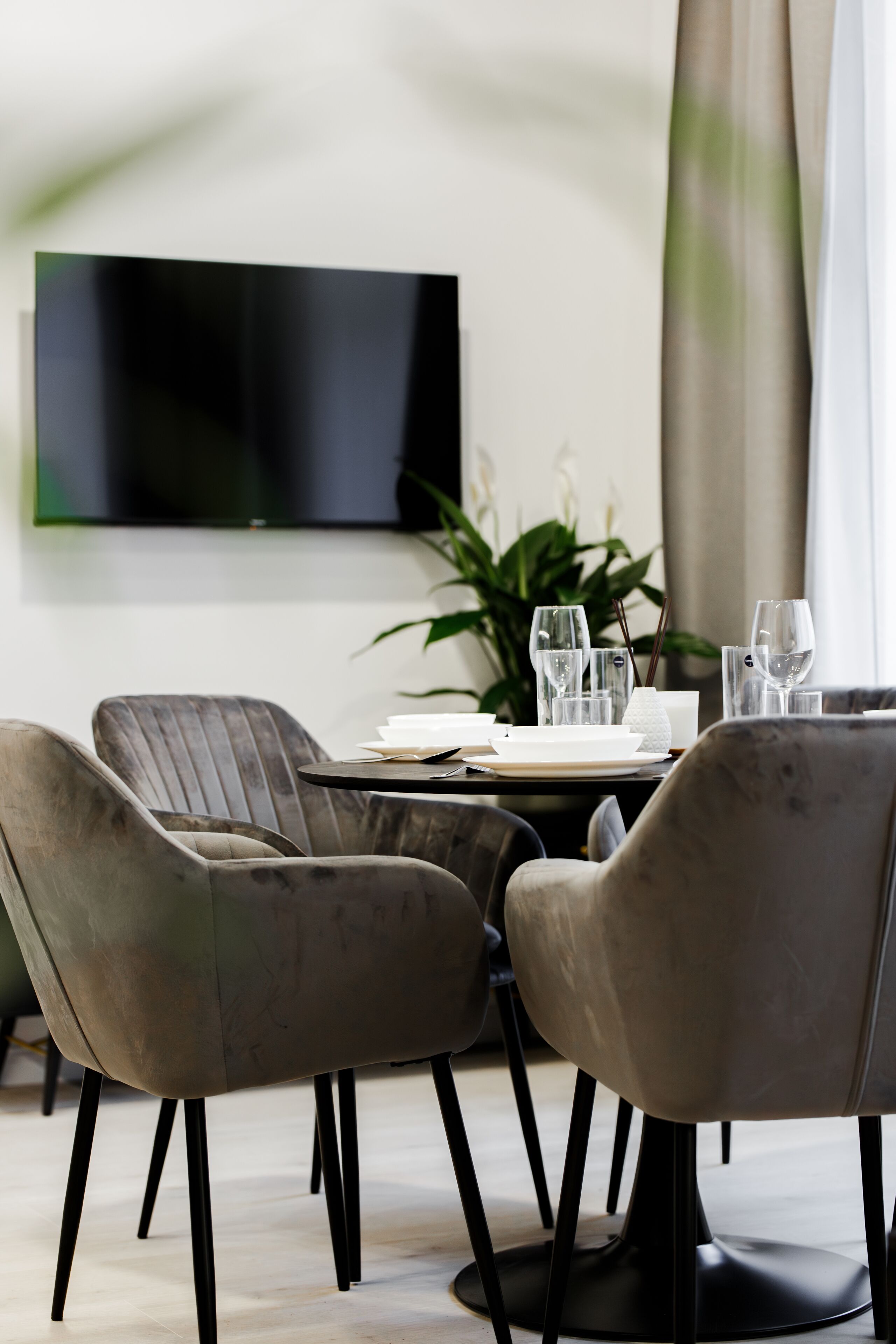 Un comedor moderno con una mesa redonda, cuatro sillas tapizadas y un televisor de pantalla plana montado en la pared.