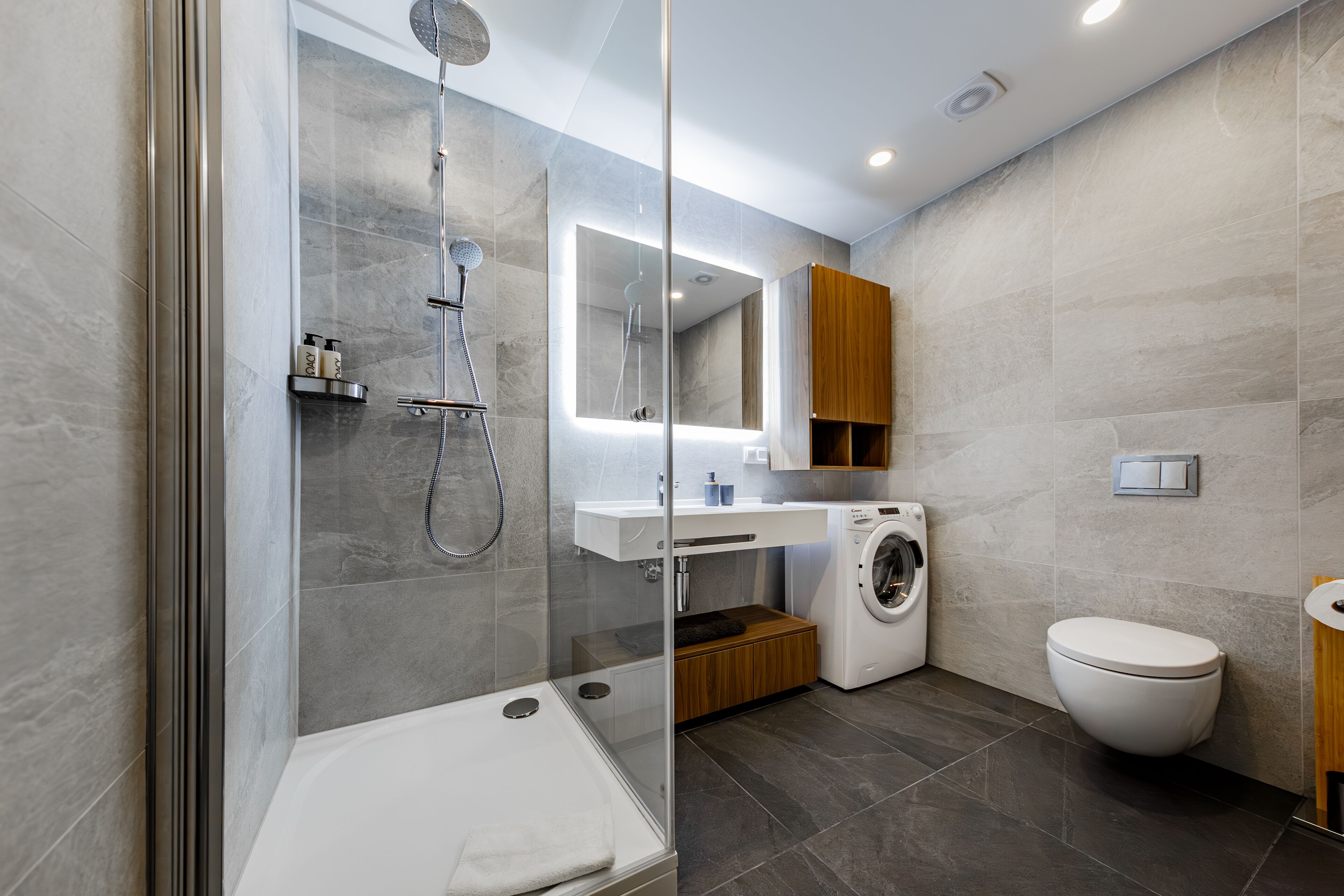 A modern bathroom with a glass-enclosed shower, a built-in washing machine, and a toilet.