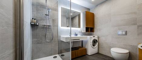 A modern bathroom with a glass-enclosed shower, a built-in washing machine, and a toilet.