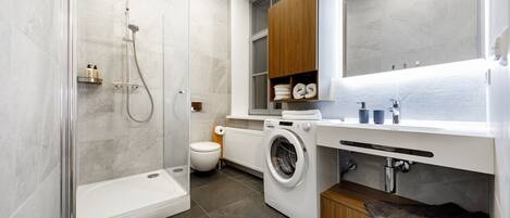 A modern bathroom with a glass-enclosed shower, a built-in washing machine, and a wooden vanity with a mirror.