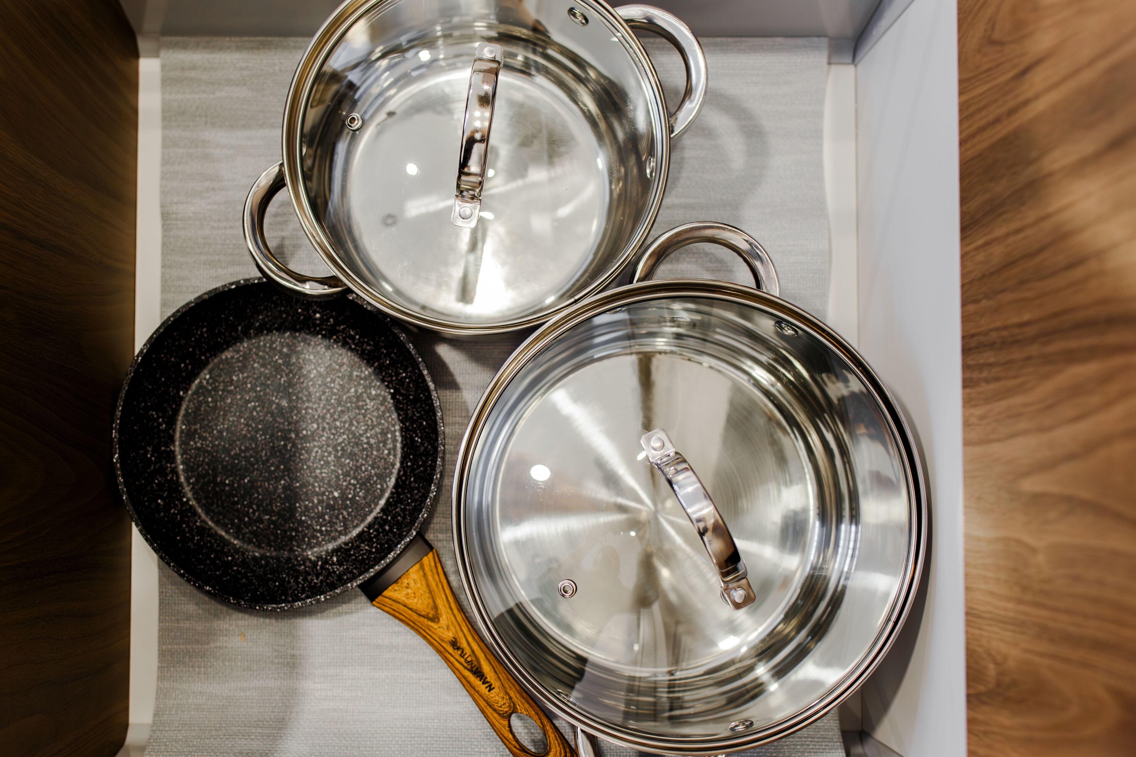 Trois casseroles avec leurs couvercles, rangées sur une étagère.