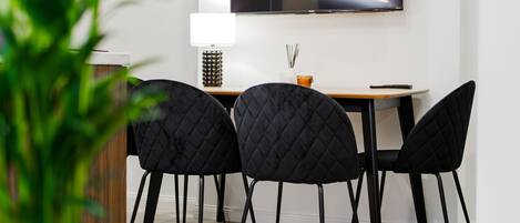 Un comedor moderno con un televisor montado en la pared, sillas negras, una mesa de madera y una planta en maceta.