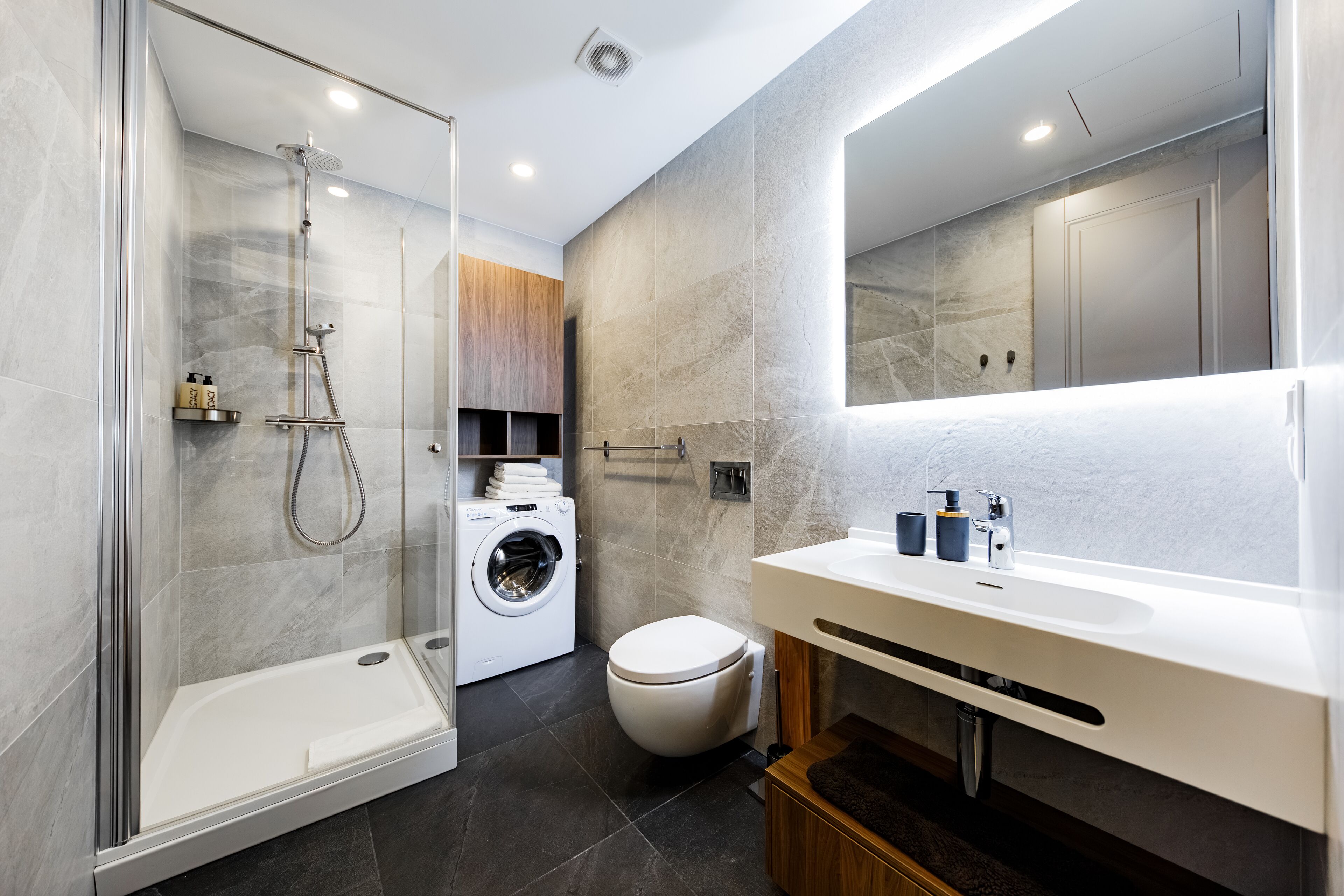 Un baño moderno con ducha de vidrio, lavadora integrada y un espejo grande sobre el lavabo.