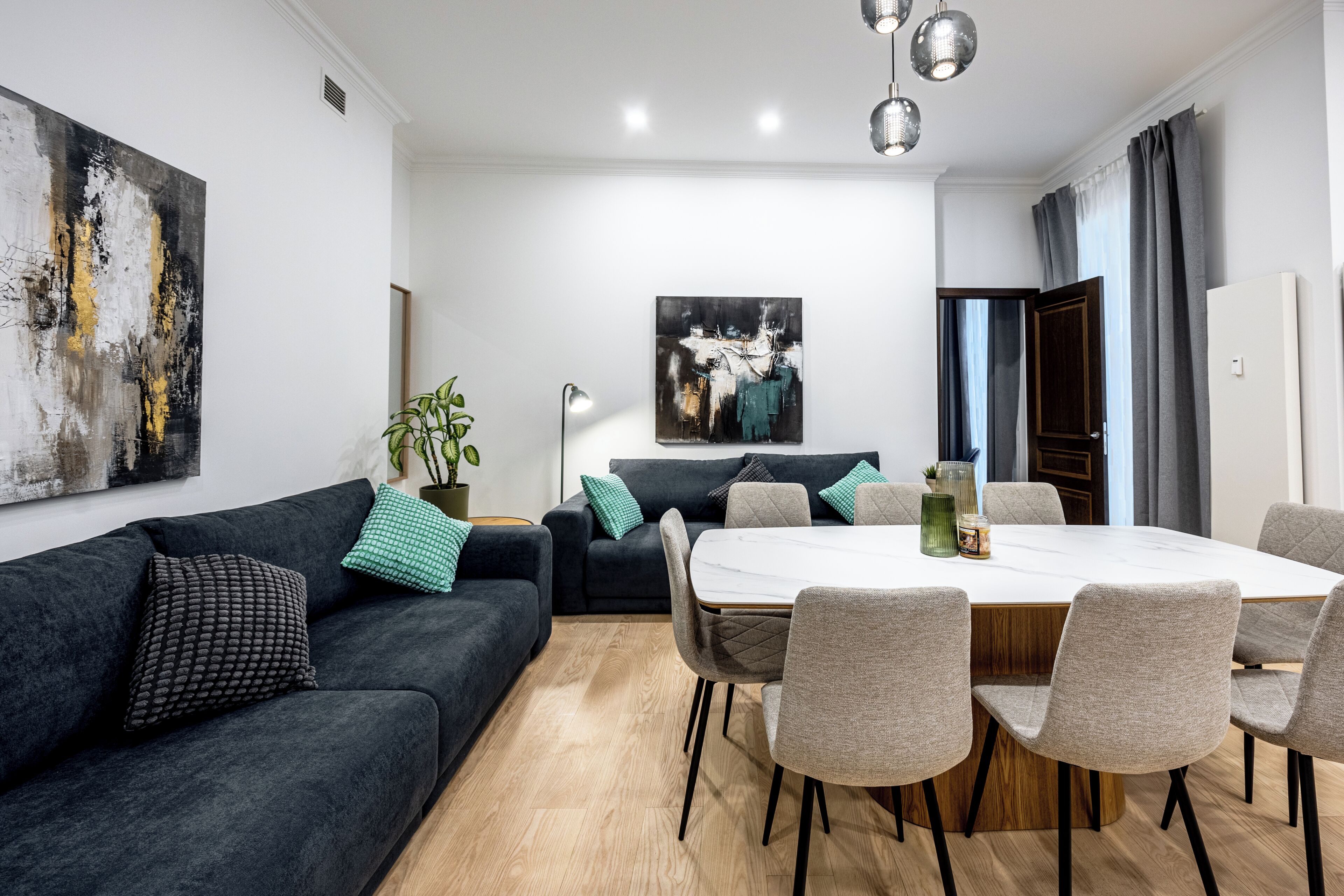 A modern living room with a dark sofa, a dining table with chairs, and a large abstract painting on the wall.