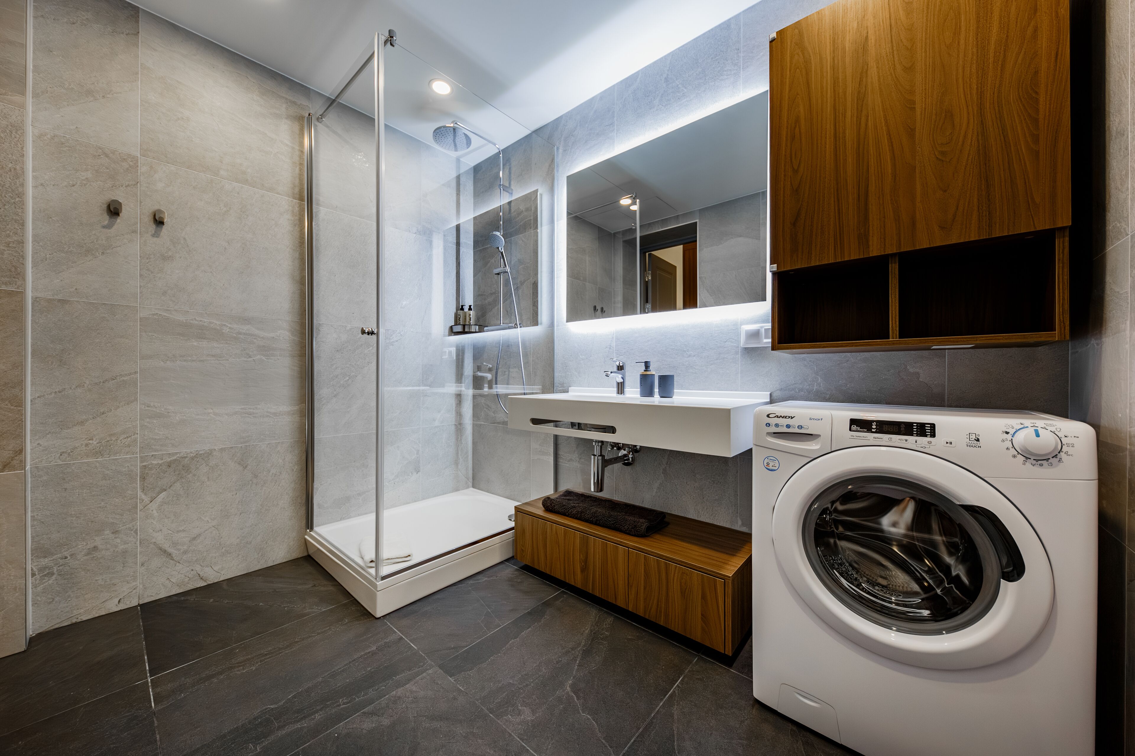 Bany modern amb dutxa de vidre, un lavabo integrat i una rentadora de càrrega frontal.
