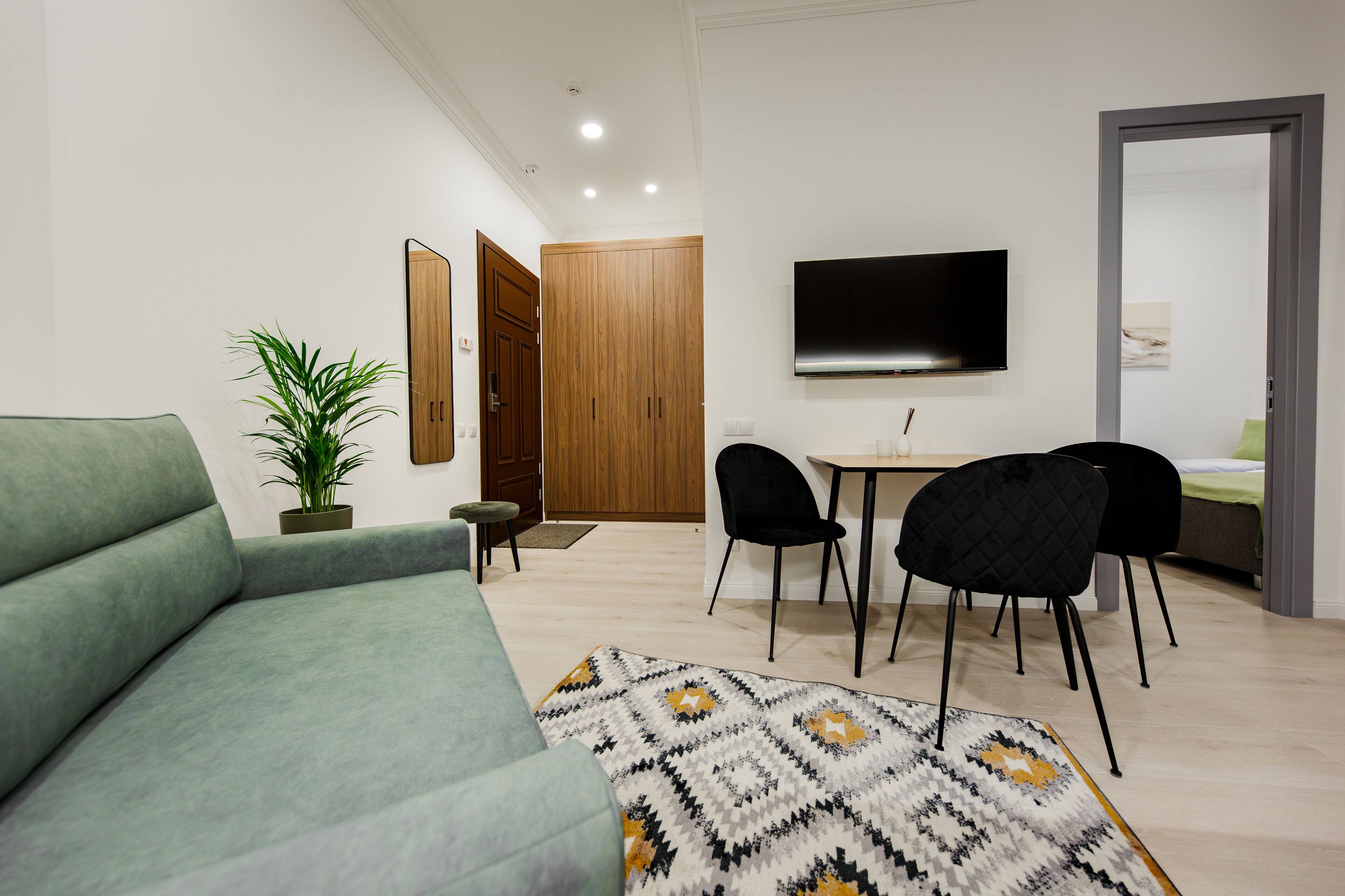Una sala moderna con un sofá verde, un tapete estampado, una mesa de comedor con dos sillas, un televisor y un armario de madera.