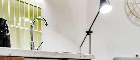 A kitchen with an open dishwasher, a wooden cabinet, a green couch, and a floor lamp.