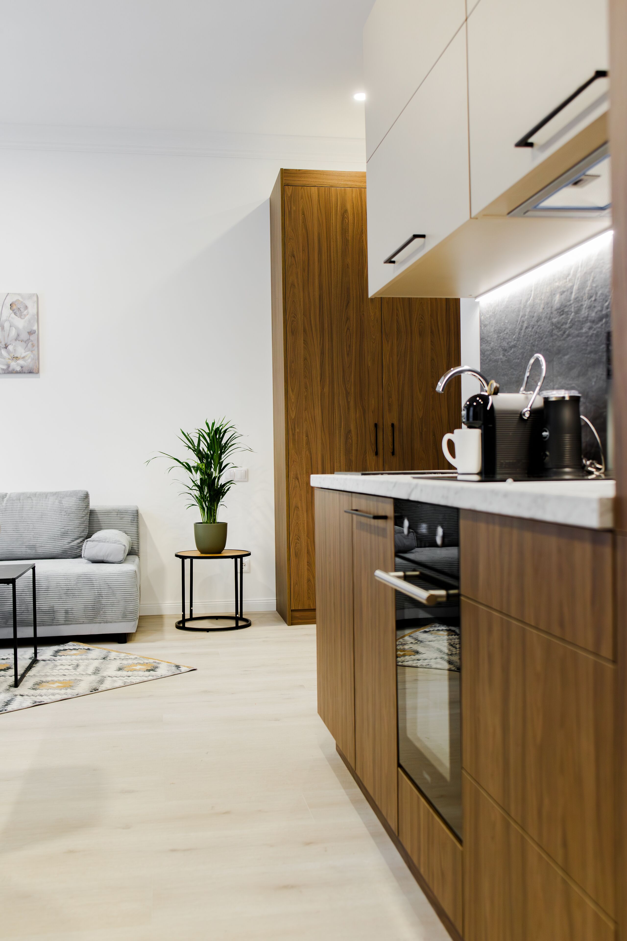 A modern kitchen with wooden cabinets, a built-in oven, and a small side table with a plant.
