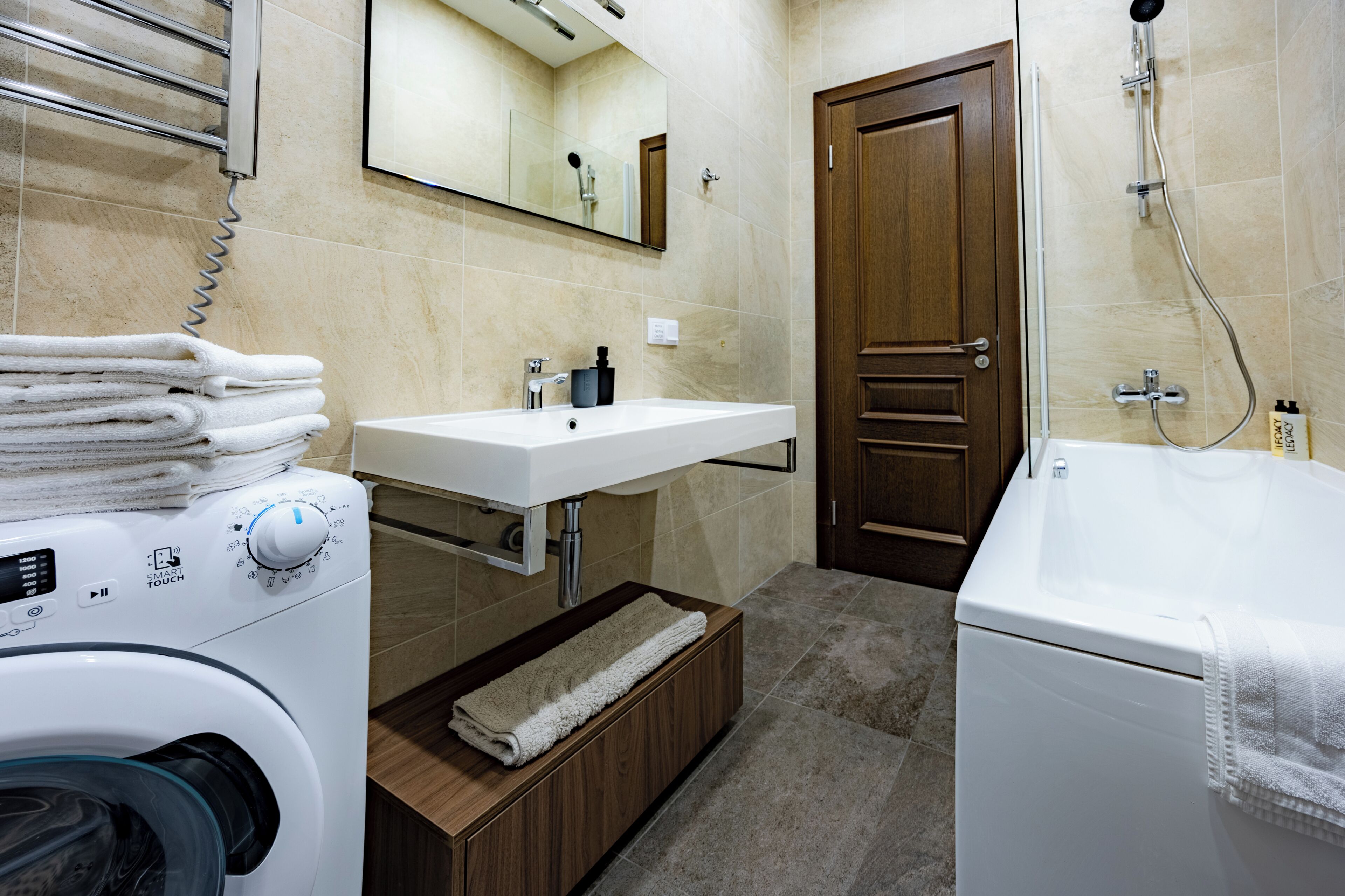 Une salle de bain d’hôtel équipée d’une machine à laver, d’un lavabo, d’un miroir, d’un meuble en bois et d’une baignoire.
