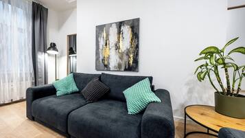 A modern living room with a dark grey sofa, a small round wooden table, a potted plant, and a large abstract painting on the wall.