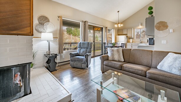 A modern living room with a fireplace, a glass coffee table, a grey armchair, and a sofa.