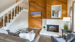 A modern living room with a staircase, a fireplace, and a large mirror.