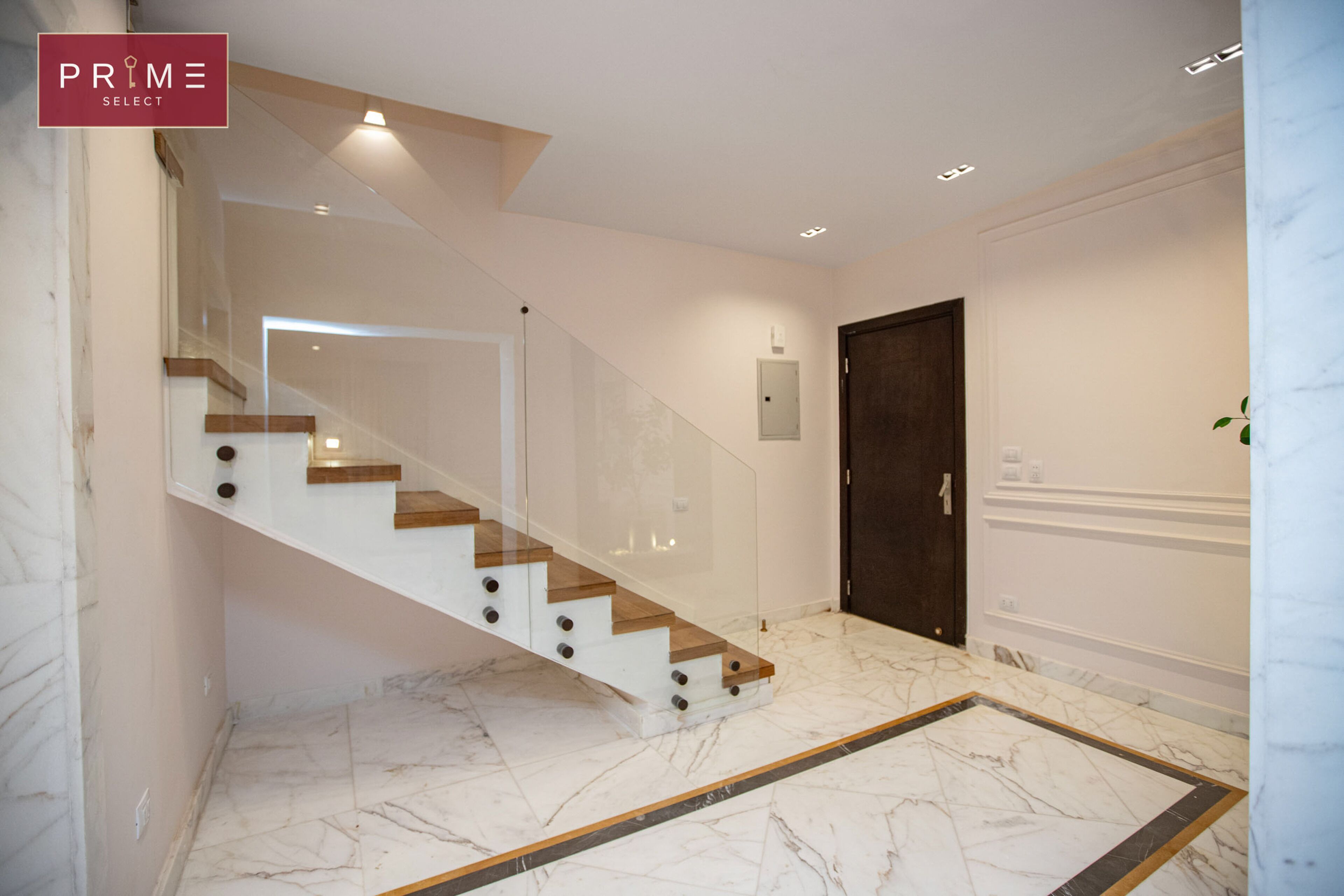 A modern interior with a marble floor, a wooden staircase, and a dark door.