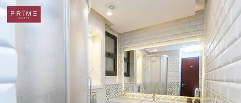 Un baño con inodoro blanco, lavamanos con espejo y azulejos decorados en las paredes.