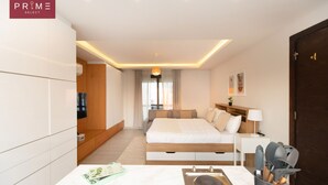 A modern hotel room with a bed, bedside table, lamp, and a view of the city.