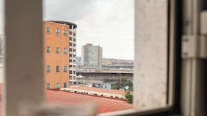 Une vue par la fenêtre sur un paysage urbain, avec des bâtiments et une structure surmontée d’un toit rouge.
