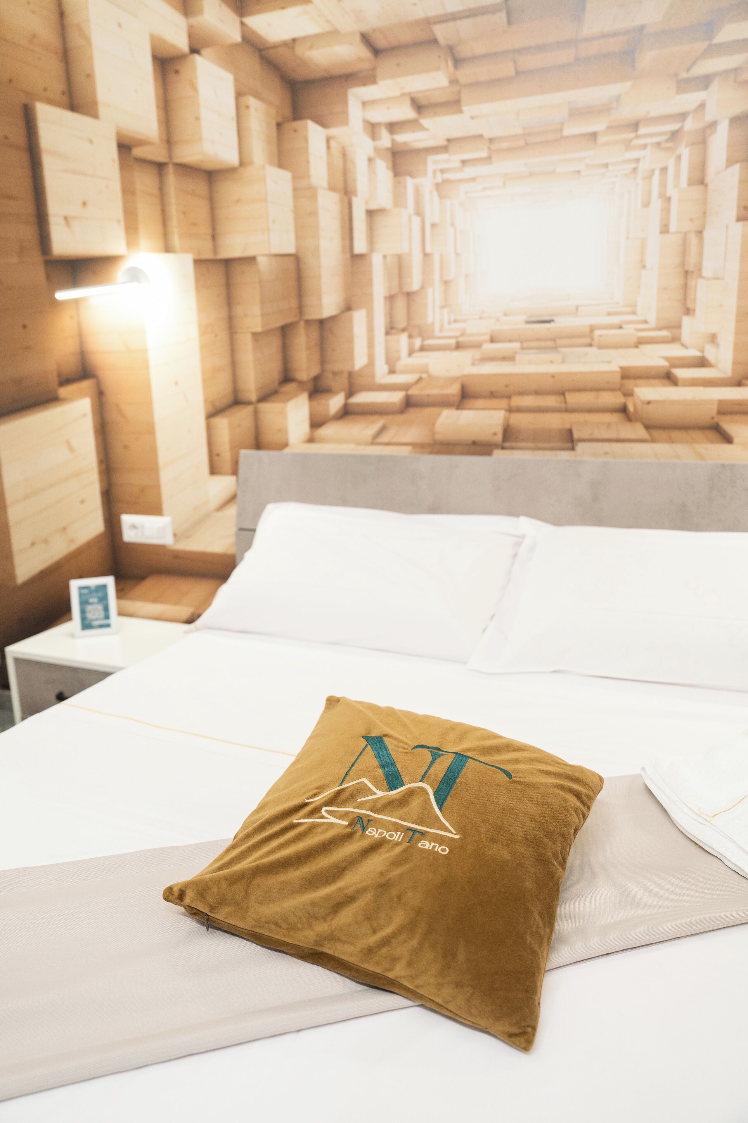 Ein ordentlich bezogenes Bett mit einem braunen und einem weißen Kopfkissen, einem Holz-Kopfseitenverkleidungen und einem Nachttisch mit Lampe.