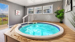 A hot tub in a room with wooden flooring, a view of the backyard, and framed pictures on the wall.
