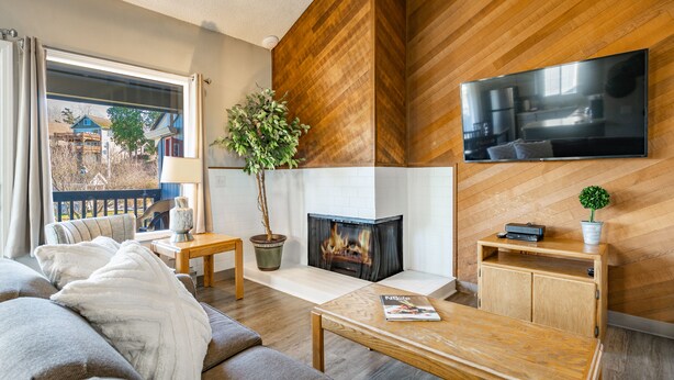 A modern living room with a fireplace, a television mounted on the wall, and a view of the outside.