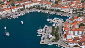 An aerial view of a marina with boats docked, surrounded by buildings with red-tiled roofs.