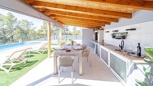 An outdoor kitchen with a dining area, a pool, and a view of the backyard.