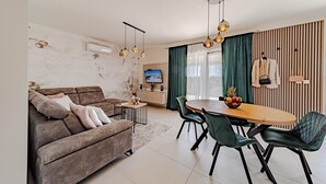 A modern living room with a sofa, dining table, chairs, and a TV.