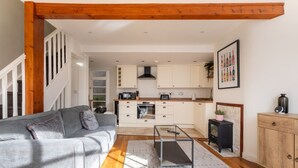 A modern living room with a grey sofa, a coffee table, and a staircase leading to a kitchen with white cabinets and a black stove. - Bright & Quirky 3BD Home - Wellington Terrace! (Bristol)