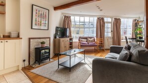 A living room with a sofa, a coffee table, a TV, a fireplace, and a window with curtains. - Bright & Quirky 3BD Home - Wellington Terrace! (Bristol)