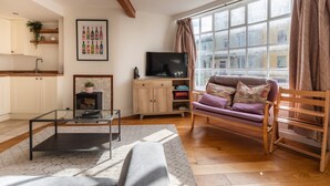 A living room with a sofa, a glass coffee table, a TV, and a fireplace. - Bright & Quirky 3BD Home - Wellington Terrace! (Bristol)