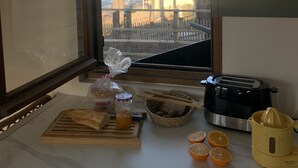 A kitchen counter with a toaster, a juicer, a cutting board with bread, a jar of jam, and a bowl of fruit. - Le Châlet, Confort à L'orée de la Forêt et la mer (Mimizan)
