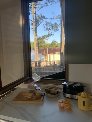 Una encimera de cocina con un tostador, un exprimidor de jugos, una tabla de cortar con pan, un tarro de mermelada y un tazón de fruta.