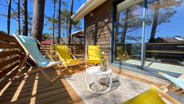 A wooden deck with lounge chairs and a small table, overlooking a forested area. - Le Châlet, Confort à L'orée de la Forêt et la mer (Mimizan)