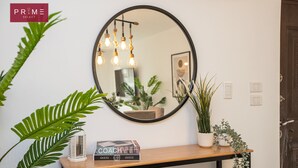 A round mirror on a wall, a wooden console table with a potted plant, a framed picture, and a book titled "COACH". - Prime Select Galleria moon valley (New Cairo)