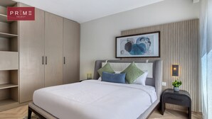 A modern bedroom with a large bed, a wardrobe, a bedside table with a lamp, and a framed artwork on the wall. - Prime Select Galleria moon valley (New Cairo)