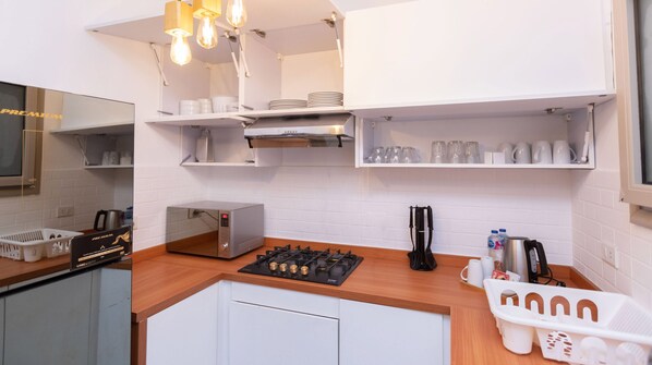 Una cocina compacta con gabinetes blancos, microondas integrado, estufa a gas y cafetera.
