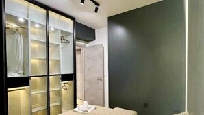 A bedroom with a large bed, a walk-in closet with glass doors, and a dark accent wall.