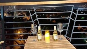 A table with wine glasses and bottles, set against a cityscape view at night.
