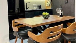 A modern dining area with a wooden table and chairs, a bowl of fruit, and a pendant light.