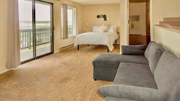 A hotel room with a large bed, a gray sofa, a balcony with a view, and a door leading to another room.