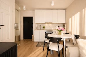 A modern kitchen with white cabinets, a black door, and a dining area with a round table and chairs. - Elite Apartments Brzeźno Family (Gdansk)