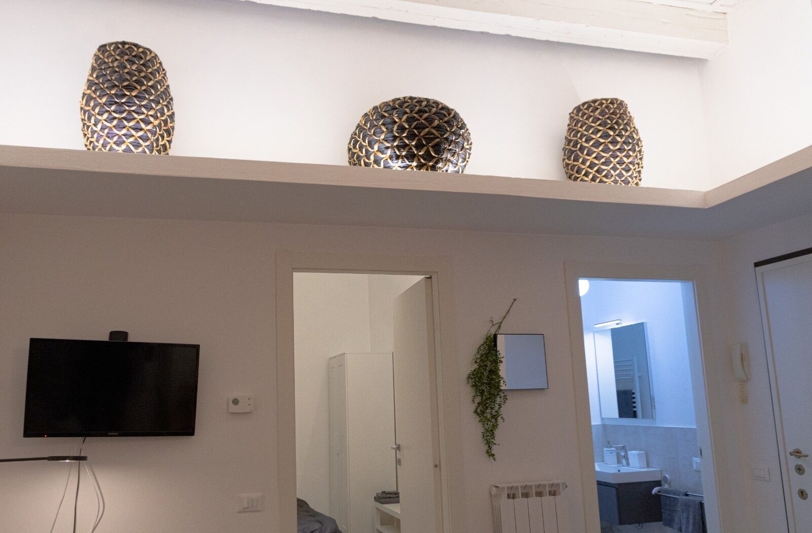 Un interior moderno con un televisor de pantalla plana montado en la pared, un acceso a un baño y lámparas esféricas decorativas en el techo.