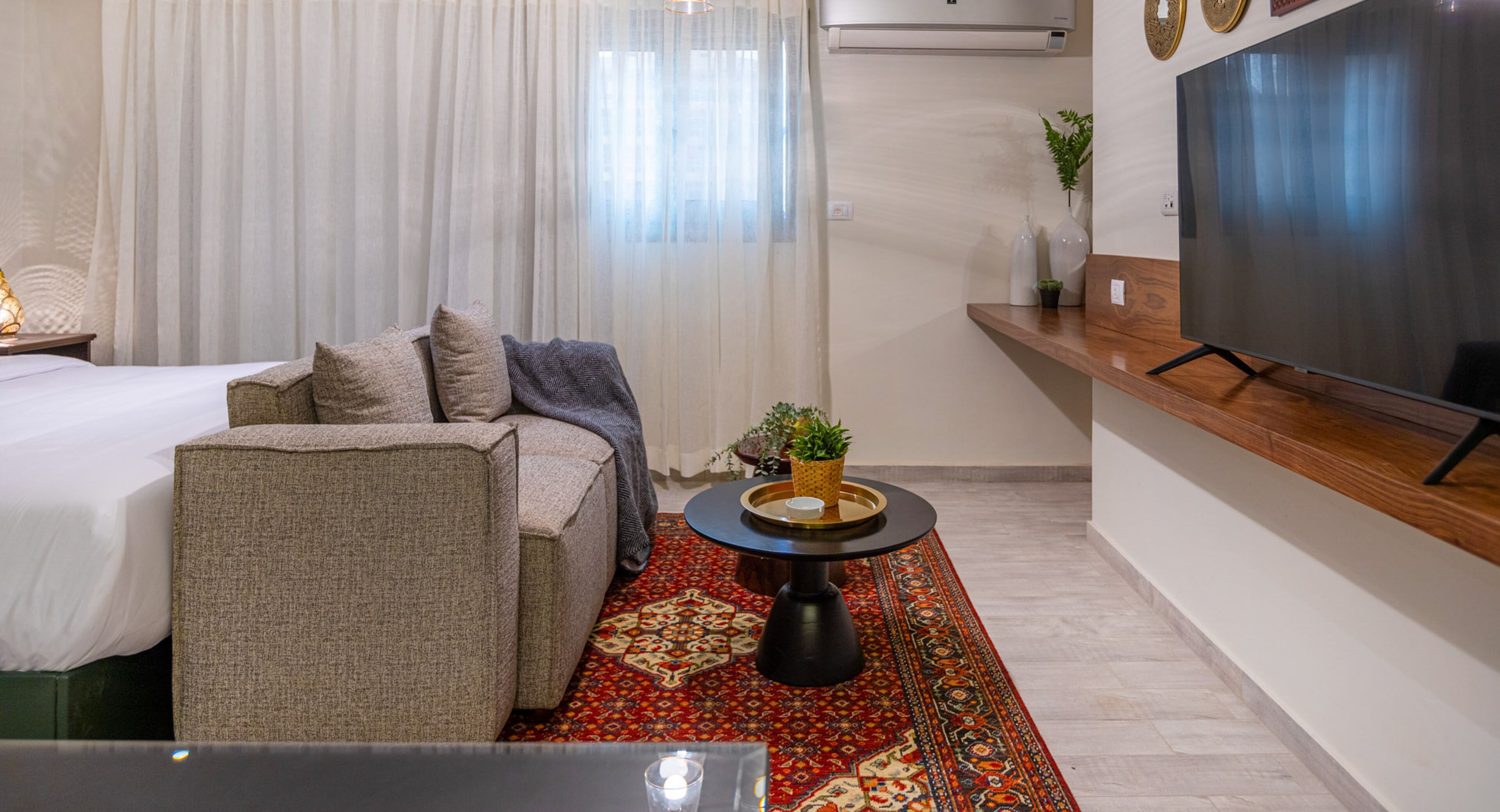A modern hotel room with a bed, sofa, TV, and a small table with a plant.